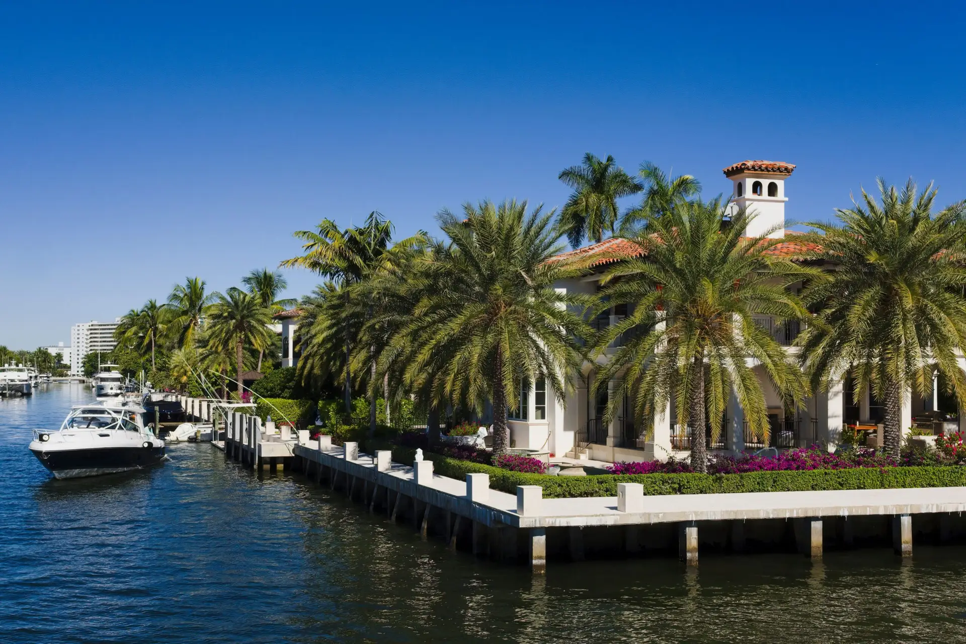 Fort Lauderdale canal-front estate with a concrete seawall cap, pilings, moored boats, and palms