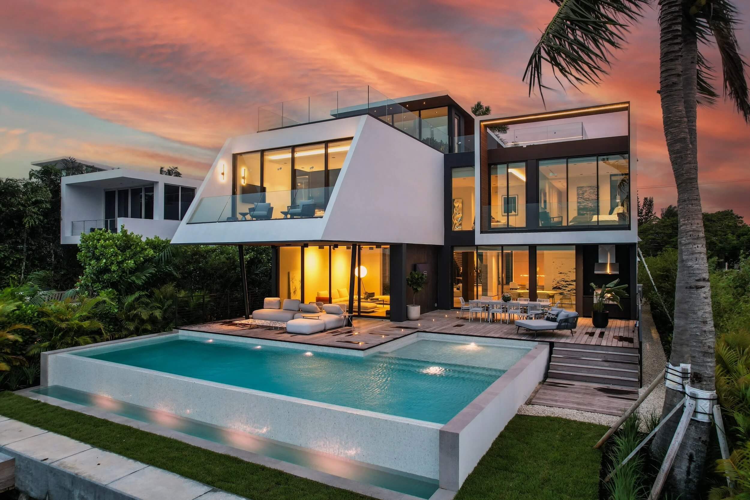 Completed modern waterfront estate at dusk with cantilevered massing, full-height glazing, and an infinity-edge pool