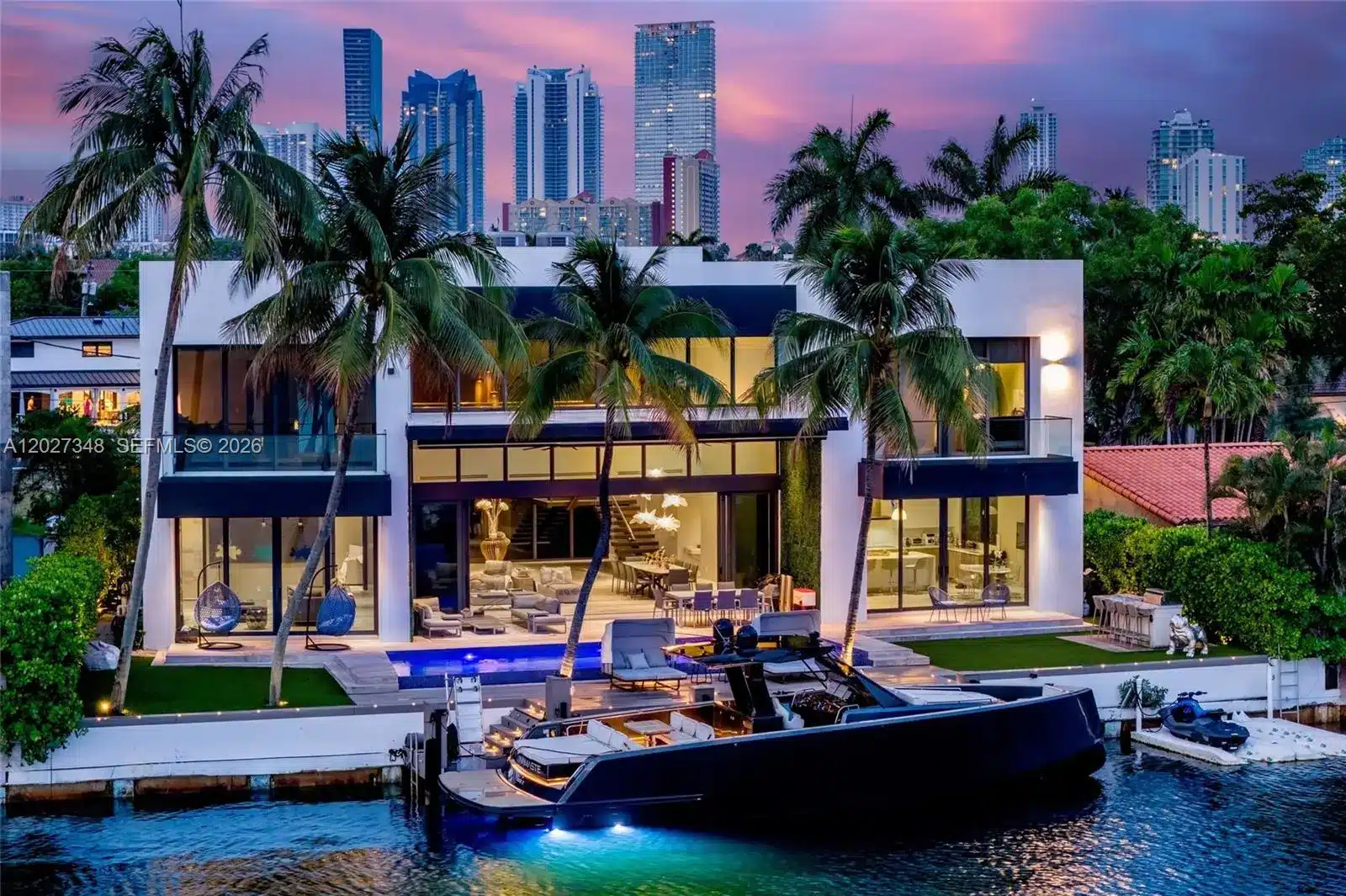 Contemporary South Florida luxury residence at dusk with a yacht moored alongside and the city skyline behind