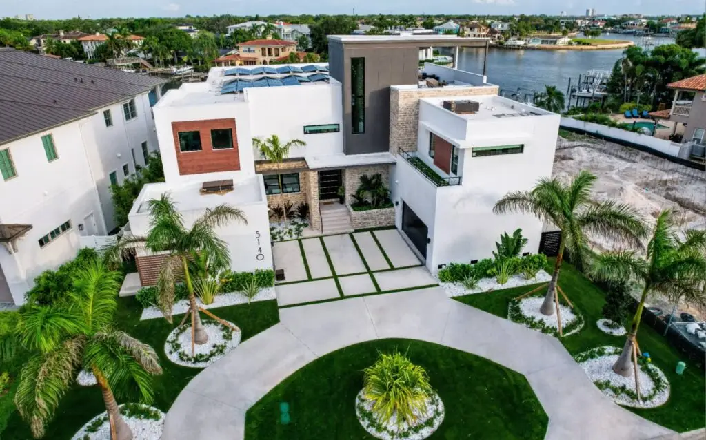 Aerial view of a contemporary white waterfront estate with circular drive and gardens