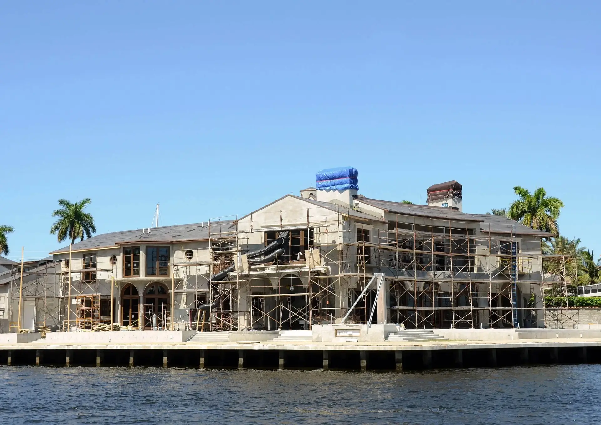 Modern vs Contemporary Architecture: What Luxury Home Buyers Mean - 2 Waterfront estate mid-construction with full scaffolding seen from the canal, structure underneath a glass-forward design